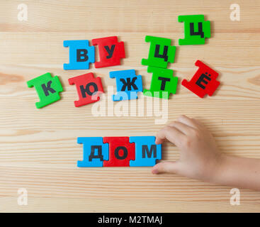 On a wooden background lie the letters of the Russian alphabet. A child spends word home in Russian.Square Stock Photo