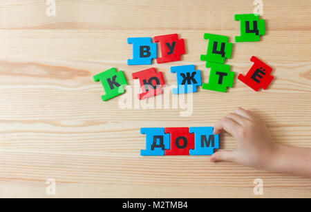 On a wooden background lie the letters of the Russian alphabet. A child spends word home in Russian Stock Photo