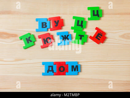 On a wooden background lie the letters of the Russian alphabet. The child laid out the inscription of the house in Russian Stock Photo