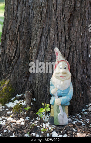 Germany, old faded garden gnome leans on a pear tree. Stock Photo