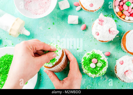 Making easter cupcakes, person decorate cakes with bunny ears and candy eggs, copy space frame top view, girl's hands in picture Stock Photo