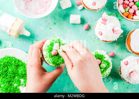 Making easter cupcakes, person decorate cakes with bunny ears and candy eggs, copy space frame top view, girl's hands in picture Stock Photo