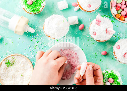 Making easter cupcakes, person decorate cakes with bunny ears and candy eggs, copy space frame top view, girl's hands in picture Stock Photo