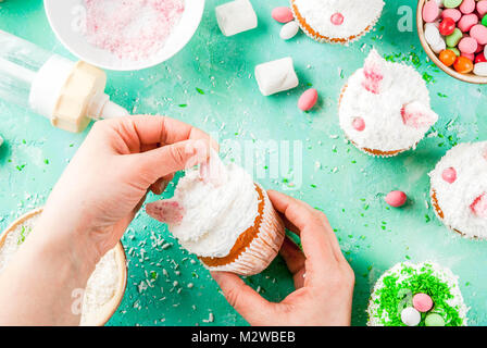 Making easter cupcakes, person decorate cakes with bunny ears and candy eggs, copy space frame top view, girl's hands in picture Stock Photo