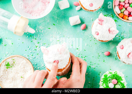 Making easter cupcakes, person decorate cakes with bunny ears and candy eggs, copy space frame top view, girl's hands in picture Stock Photo