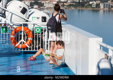 Corsica, France - July 2, 2015: Young mother takes photo on a smartphone from passenger ferry deck, children sit on deck Stock Photo
