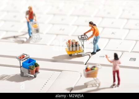 Miniature people shopping for various items with carts on a white computer keyboard in a concept of online shopping with focus to a man in the center Stock Photo