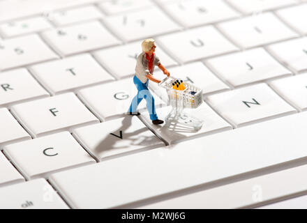 Miniature figurine of a shopper pushing a trolley over a computer keyboard in a concept of online or internet shopping Stock Photo