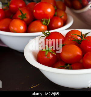 Whole cherry tomatoes in a white porcelain bowl on brown wooden table Stock Photo