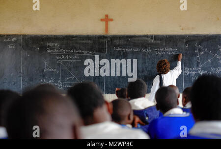 Kibuye/Rwanda - 08/26/2016: Teacher and pupils at mathematics lesson in a classroom in a school in Africa. A blackboard and cross can be seen in the b Stock Photo