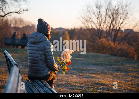 Sitting girl in the park looking the horizon at sunset with flower in her hand - happy traveler enjoying sunshine view - Freedom concept. Stock Photo