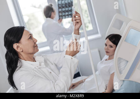 Joyful female medical worker adjusting drop counter Stock Photo