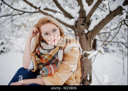 Portraiy of blonde girl in glasses, red fur coat and scarf at winter day. Stock Photo