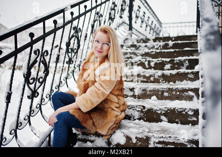 Portraiy of blonde girl in glasses, red fur coat and scarf at winter day. Stock Photo