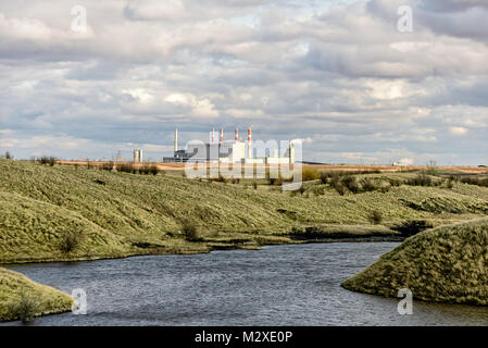 The building of a power plant with smoking pipes in the background, a blue river and green grass in the foreground, Stock Photo