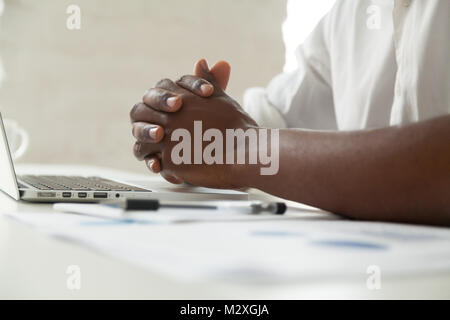 Clasped male black hands on office desk close up view, attentive african american businessman in closed posture, tension or nervous anticipation, dete Stock Photo