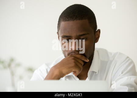 Focused african american manager working on laptop thinking hard of problem solution, concentrated black businessman concerned about work task, busy s Stock Photo