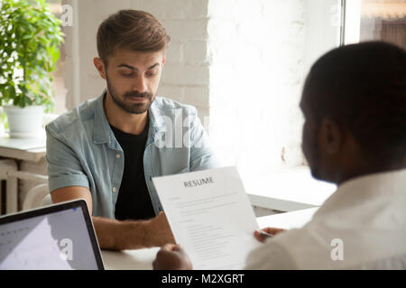 Stressed caucasian applicant feels worried while african hr employer reading resume, stress at job interview concept, nervous anxious man candidate wa Stock Photo
