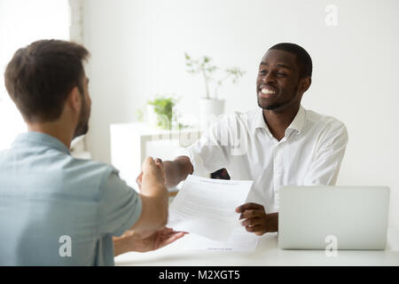 African employer handshaking new hire caucasian employee holding Stock Photo
