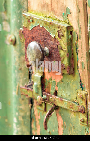 a rusty old vintage door handle on an old garden shed with rusty lock and peeling paintwork in a shabby chic style. garden shed outbuilding latch lock Stock Photo