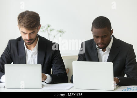 Focused busy diverse businessmen working on laptops sharing offi Stock Photo