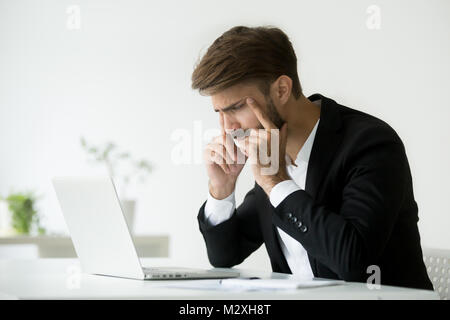 Businessman squinting eyes trying to focus looking at laptop scr Stock Photo