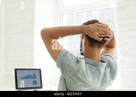 Rear view at man looking at statistics on laptop screen Stock Photo
