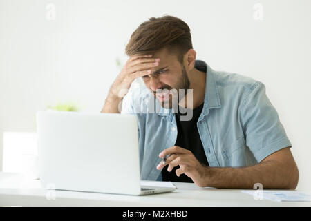 Confused young man frustrated by online problem looking at lapto Stock Photo