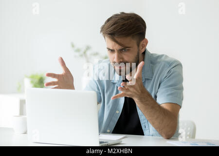 Angry man disagree with fake online news looking at laptop Stock Photo