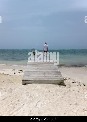 Young man walking to end of bleached wooden board jetty off Bodden Town Road, Grand Cayman, Cayman Islands. Stock Photo