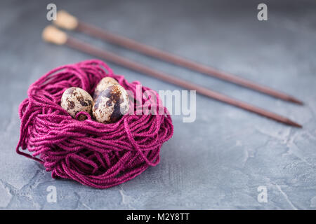 Quail eggs in a violet colorful wool nest with knitting needles. Knitters easter postcard concept. With a copyspace Stock Photo