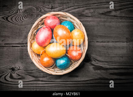 Multicolor Easter eggs in a basket on a wooden background. Stock Photo