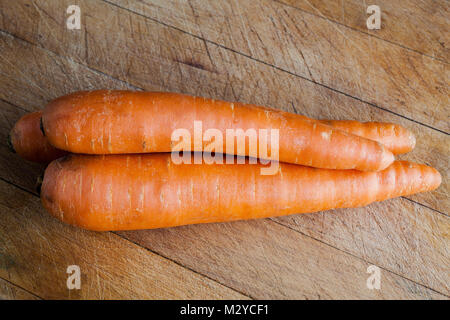 Three raw carrots on wooden cutting board Stock Photo