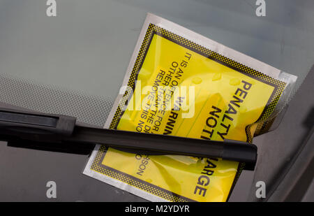 A yellow penalty charge notice underneath a car windscreen wiper Stock Photo