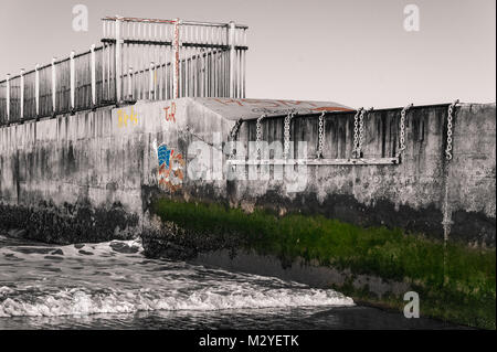 Black & White Photo of a Beach Jetty on the California Coast with graffitis and green moss in colors at Dockweiler State Beach in Playa del Rey, CA. Stock Photo