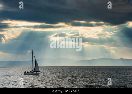 Sailing boat before the sun breaking through the clouds above the Amur in Vladivostok, Russia Stock Photo