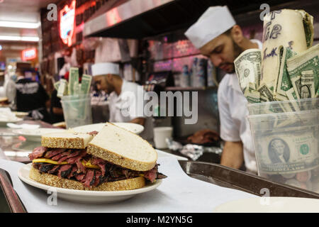 Hard-working staff making pastrami sandwiches in the open kitchen at Katz's Delicatessen, a famous New York City restaurant. Tips in cup on counter. Stock Photo