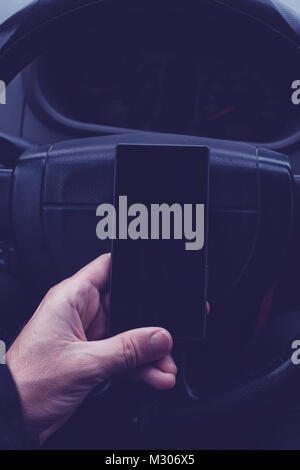 Man using mobile phone in car. Male hand with modern smartphone over steering wheel, ultra violet toned shadows Stock Photo