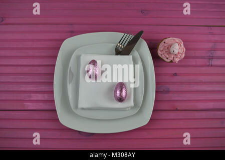 Easter time table place setting in white with cupcake and Easter egg decorations Stock Photo