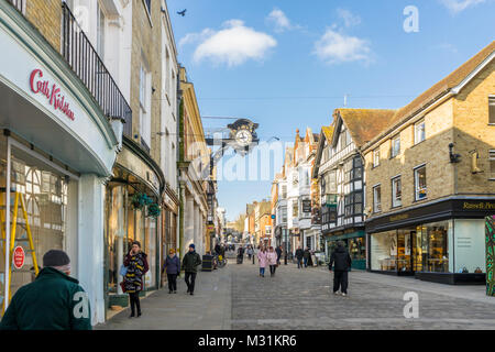 People walking along Winchester High Street with Winchester high street clock on a bright day with blue sky in Winchester 2018, Hampshire, England, UK Stock Photo