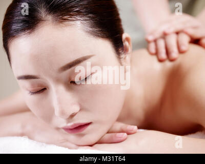 close-up of face of a beautiful young asian woman lying on front on bed receiving massage in spa salon. Stock Photo