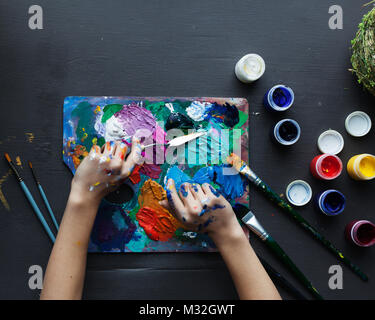 The artist's hands, paint palette brushes, different colors. The girl is drawing. The artist's tools for real art and inspiration. Dark light. Top Vie Stock Photo