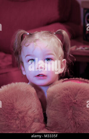 13-month old girl staring out from behind the upside-down large stuffed bear she is carrying around Stock Photo