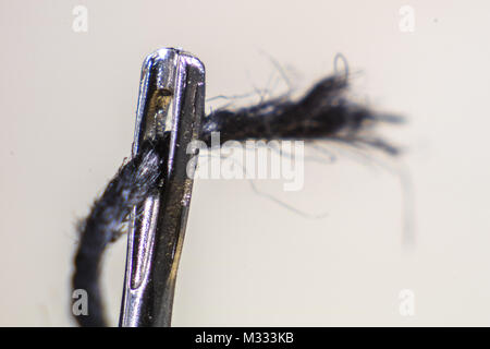 The ear of a sewing needle with a thread. The thread is threaded through the ear of the tailor's needle. Sewing accessories. Stock Photo