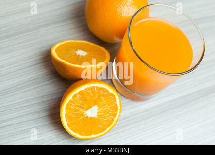Glass of squeezed orange juice. Fresh and juicy oranges on the wooden table. Stock Photo