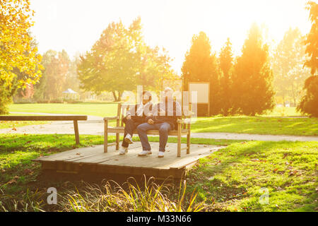 Beautiful smiling senior couple sitting on wooden bench in park at sunset. Concept Love Family Stock Photo
