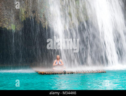 Smiling woman sitting on a raft under a waterfall in lotus position, Moalboal, Philippines Stock Photo