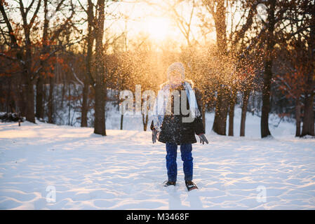 Boy standing in forest throwing snow in the air Stock Photo