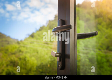 Close up door handle on opened black modern glass door with green natural and blus sky background. Stock Photo