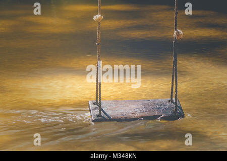 Relaxation Concept : Wooden swing hanging on tree above the water stream at outside resort in vintage style. Stock Photo